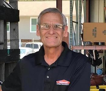Caucasian Man wearing glasses, and black collar shirt with Servpro logo. Smiling showing teeth