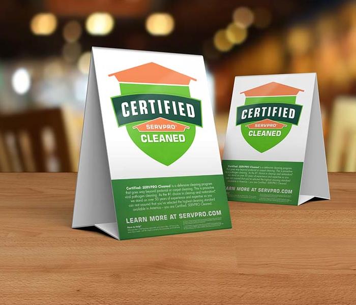 Table tent signs describing the Certified: SERVPRO Cleaned program on top of a wooden table.